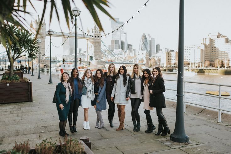 a group of young women standing next to each other on a sidewalk near the water