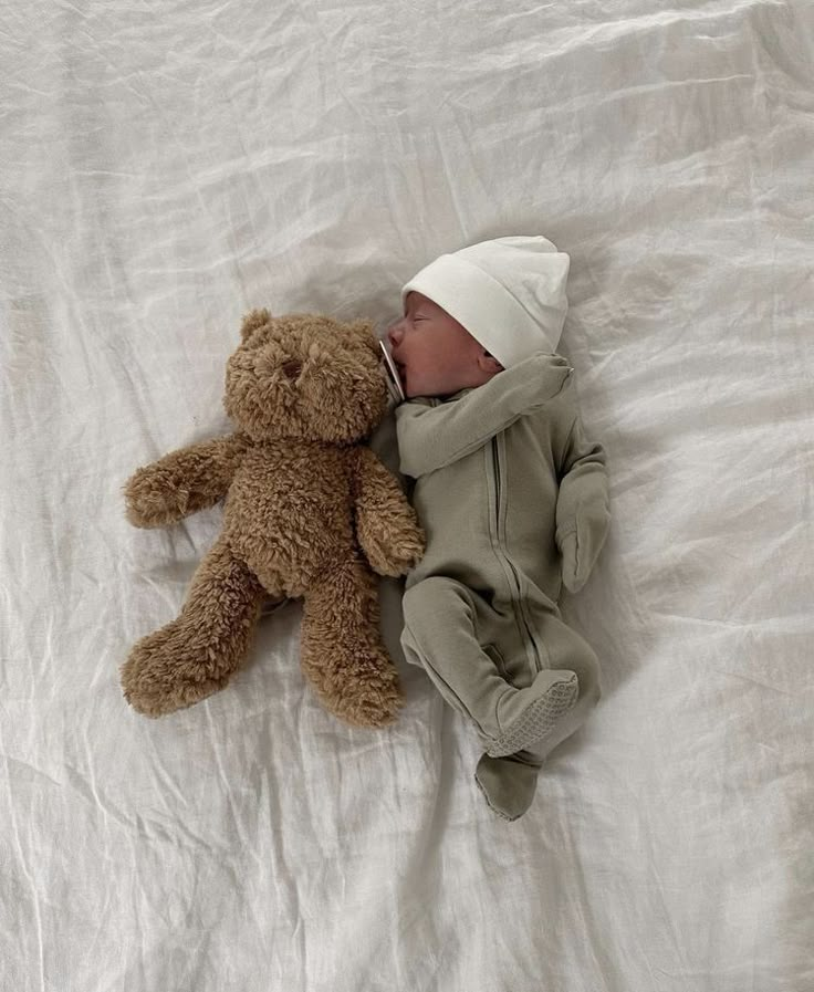 a baby sleeping next to a brown teddy bear