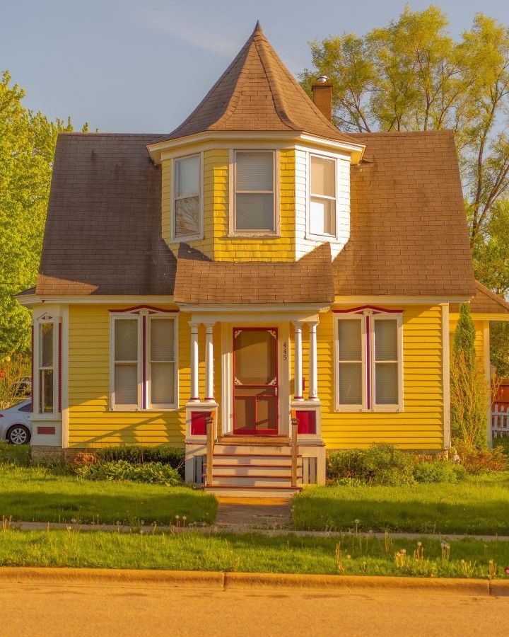 a yellow house with a red door and two windows