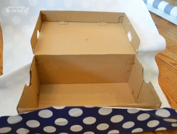 an open cardboard box sitting on top of a wooden table next to a blue and white polka dot ribbon