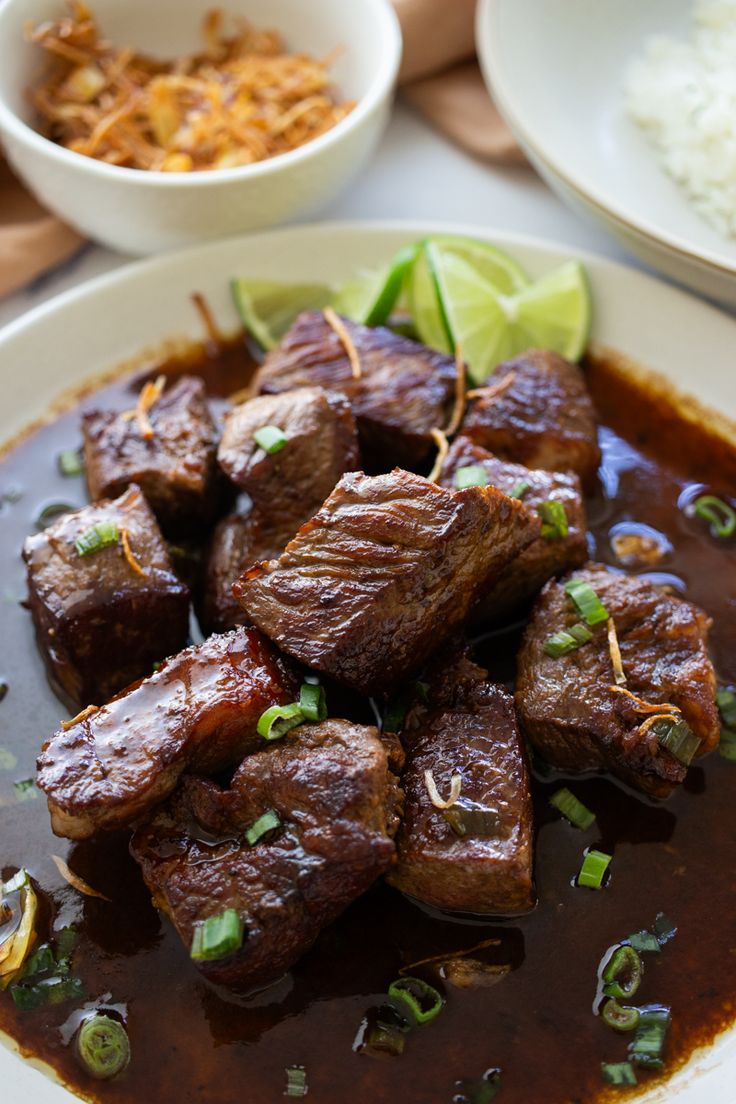 some meat and sauce on a white plate with rice, limes and cilantro