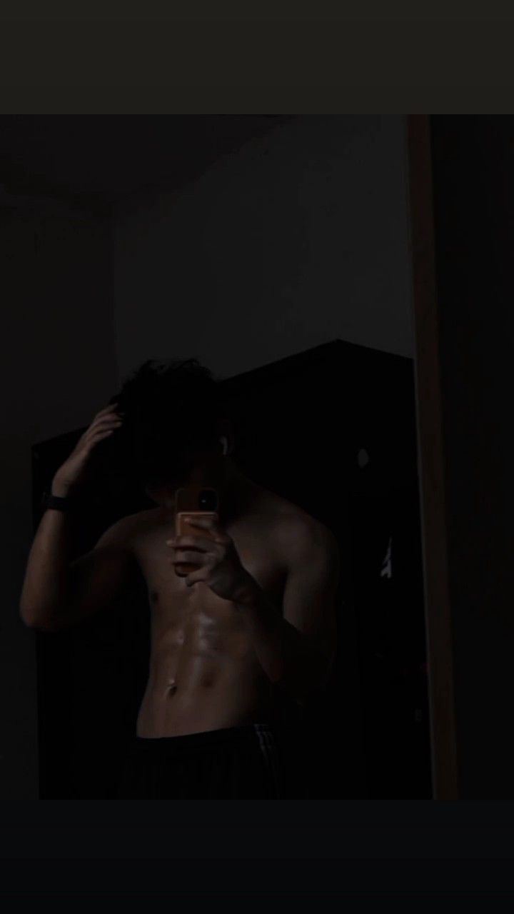 a shirtless man taking a selfie with his cell phone in the dark room