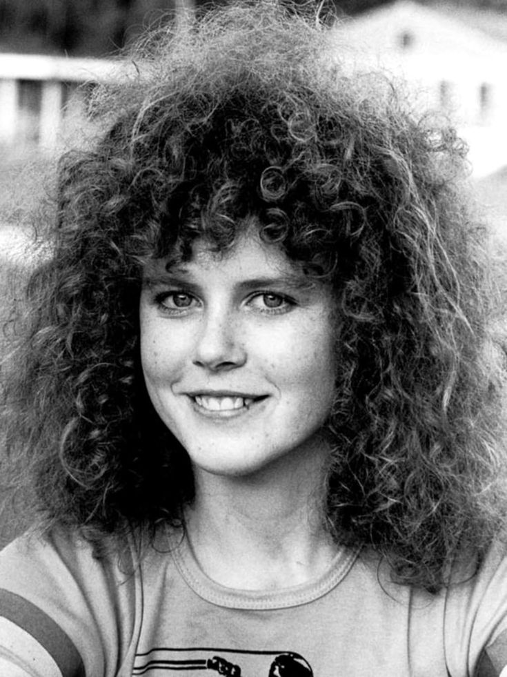 black and white photograph of a woman with long curly hair wearing a t - shirt