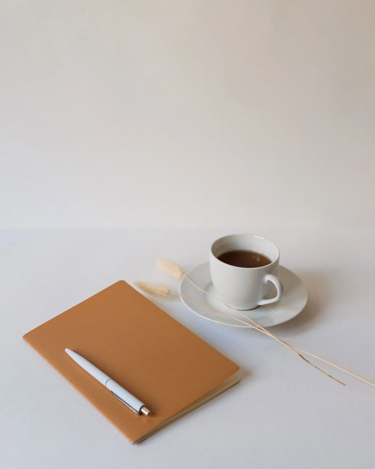 a cup of coffee next to a notebook and pen on a white table with a plain background