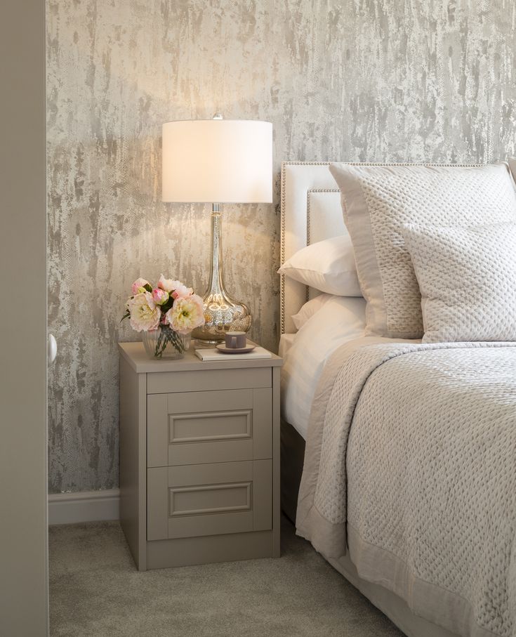 a white bed sitting next to a night stand with flowers on it and a lamp