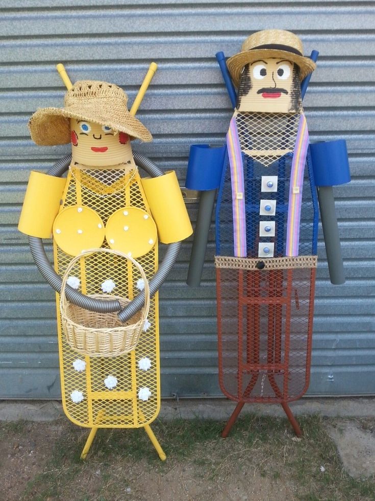 two wooden figures standing next to each other in front of a garage door, one holding a basket and the other wearing a straw hat