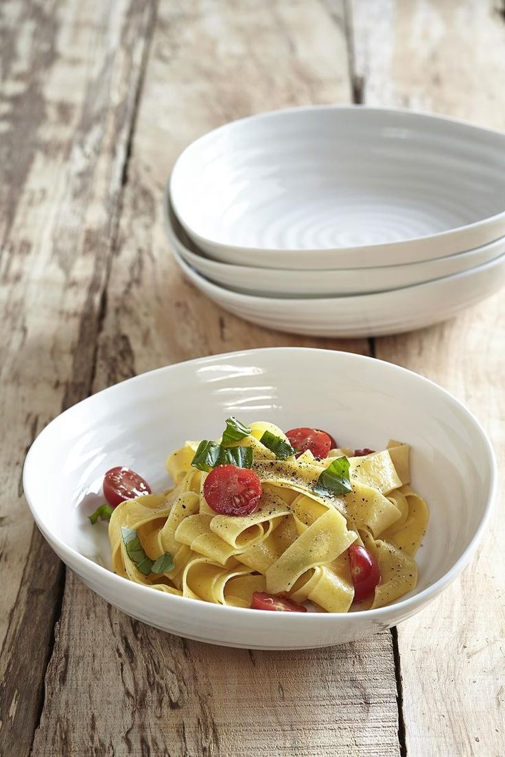 two bowls filled with pasta and vegetables on top of a wooden table next to each other