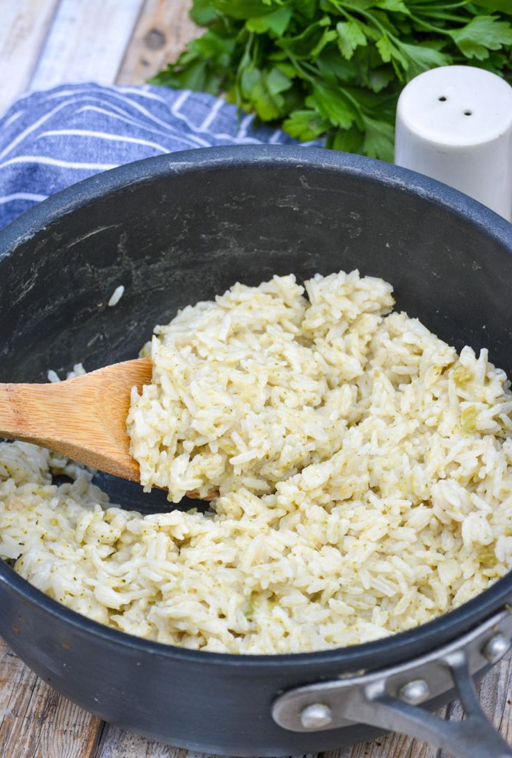 rice is being cooked in a pot with a wooden spoon on the side and parsley next to it