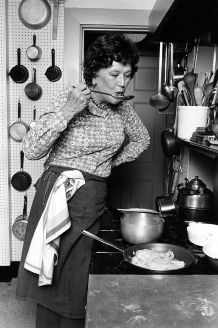 an old black and white photo of a woman cooking in the kitchen with her spoon