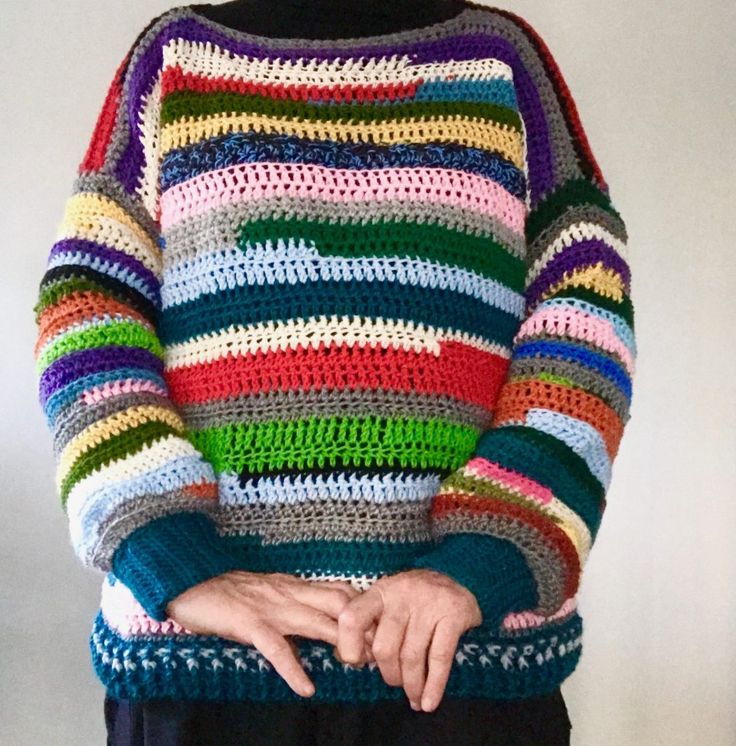 a woman wearing a multicolored crocheted sweater with her hands on her hips