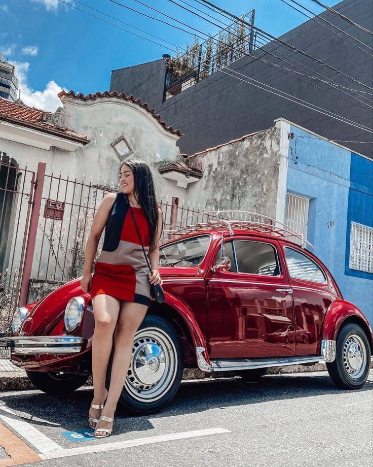 a woman sitting on the hood of a red car in front of a blue building