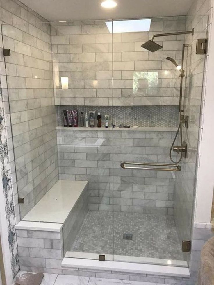 a walk in shower sitting next to a white tiled wall and floor with glass doors