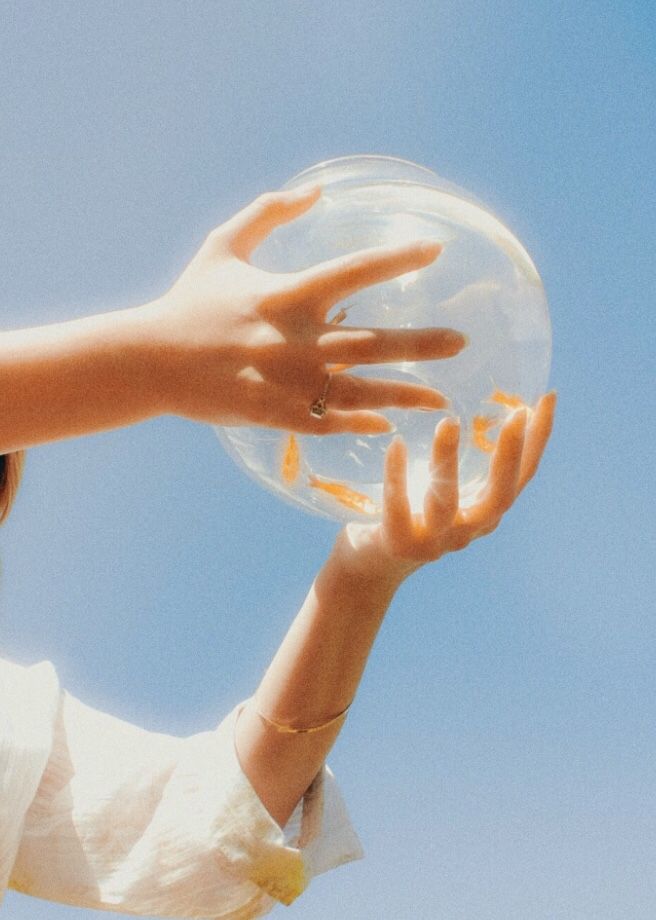 a woman holding a bubble ball with her hands in the air, against a blue sky