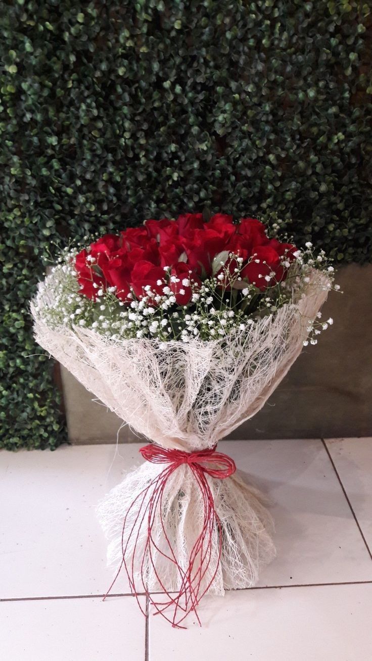 a bouquet of red roses wrapped in white paper and tied with twine on a tile floor