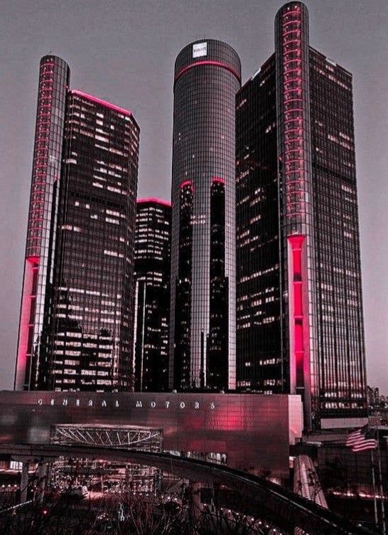 the tall buildings are all lit up in red and black colors at night, along with a bridge leading to them