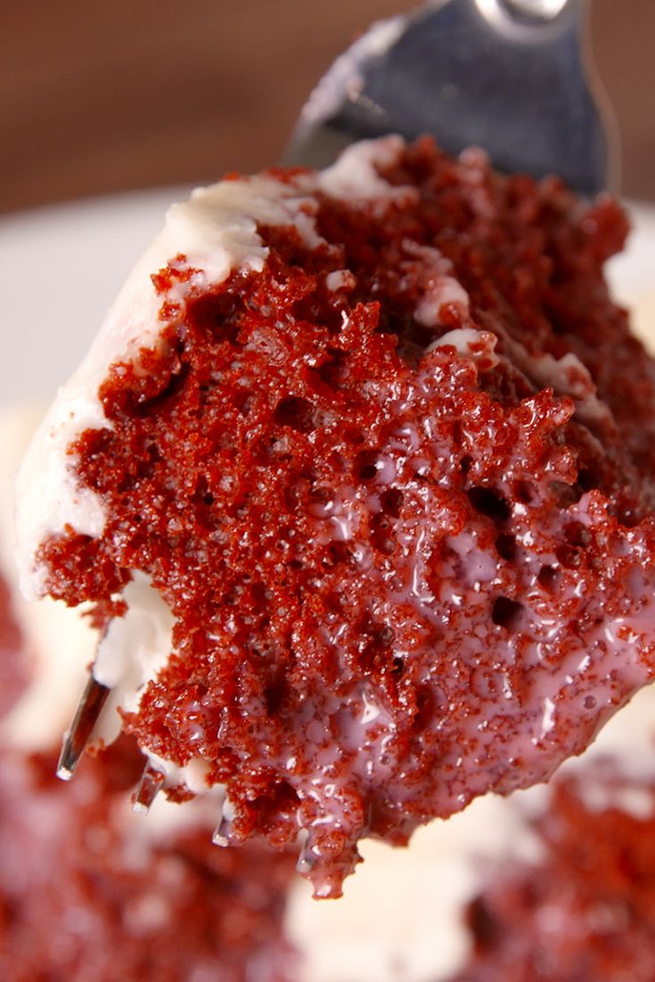 a piece of red velvet cake with white frosting and a fork in the foreground