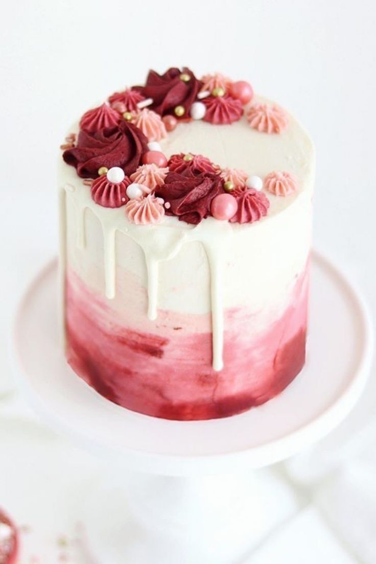 a white and red cake with icing on top sitting on a plate next to other desserts