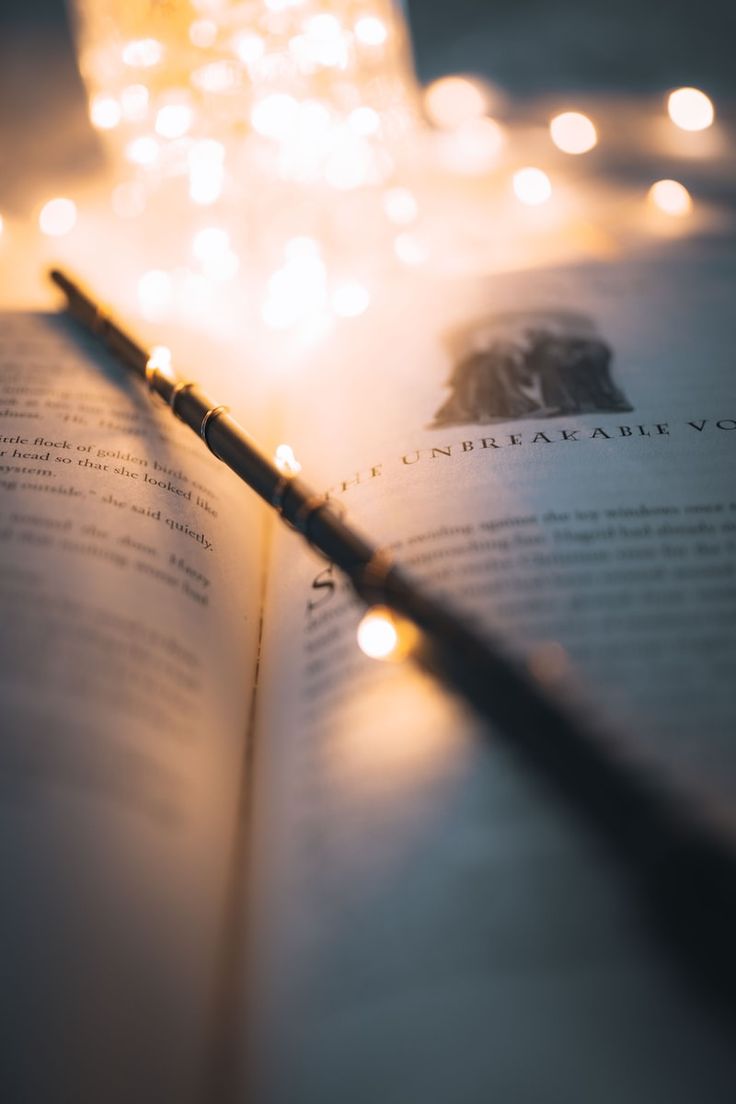 an open book with a harry potter wand laying on it's side next to some candles