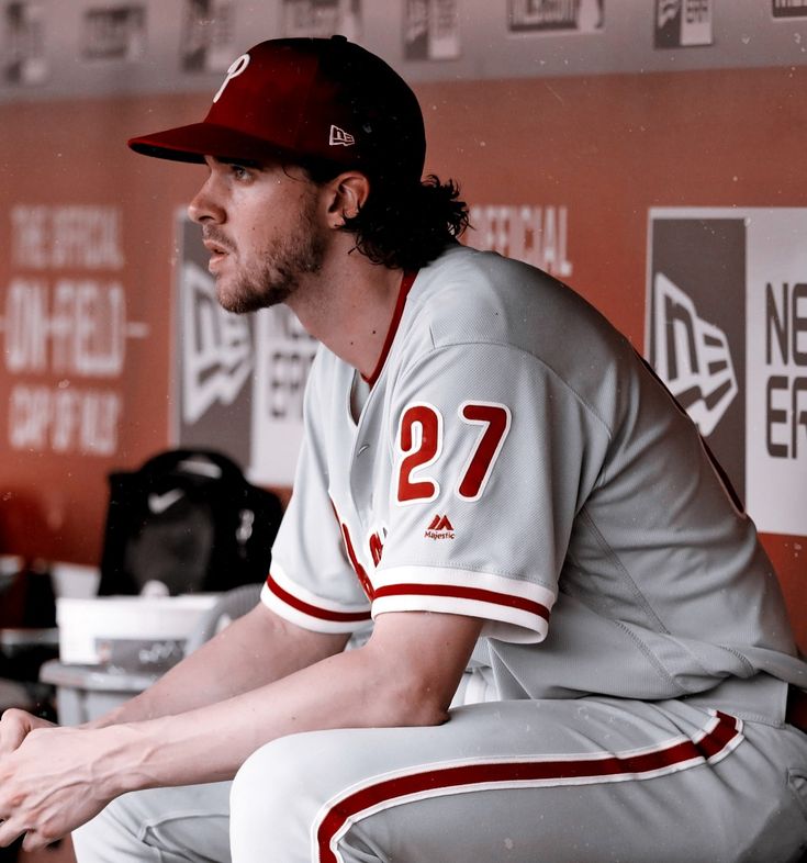 a baseball player sitting in the dugout with his hands on his knees and looking off to the side