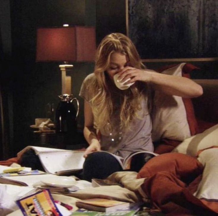 a woman sitting on top of a bed next to a book and cup filled with liquid