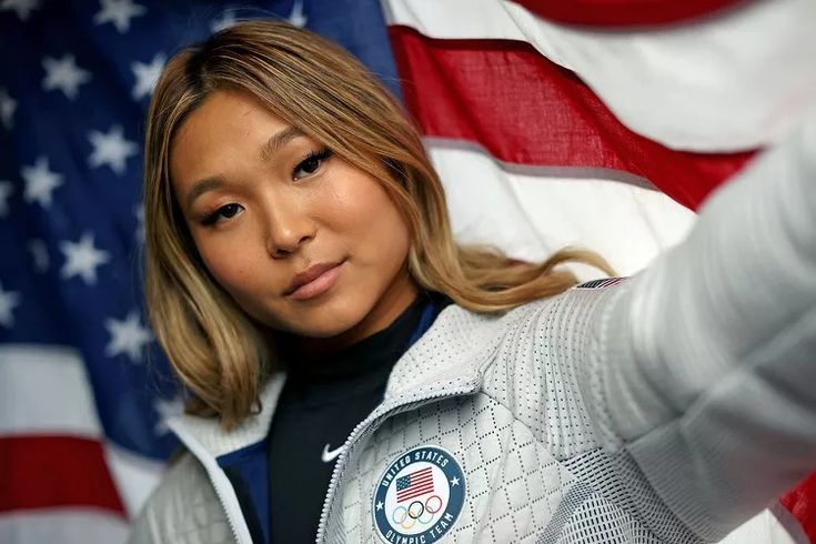 a woman in front of an american flag pointing at the camera with her finger up