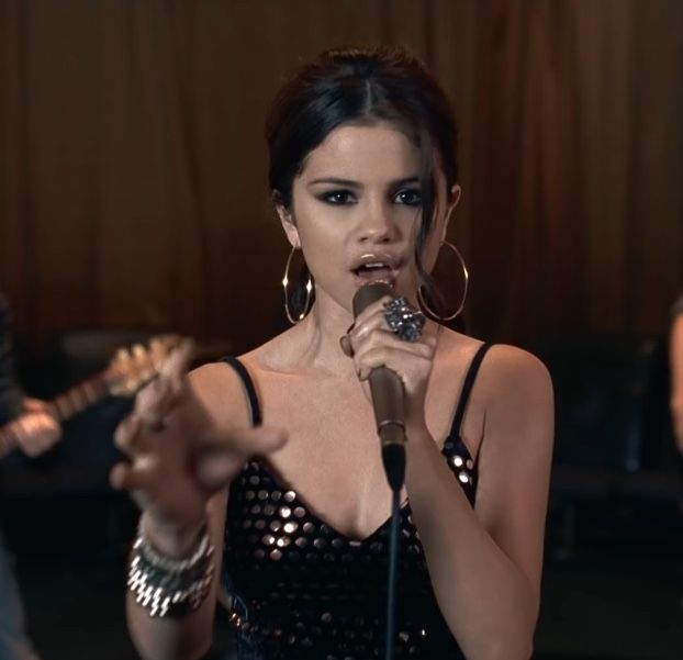 a woman holding a microphone in her right hand and singing into the microphone with two other people behind her