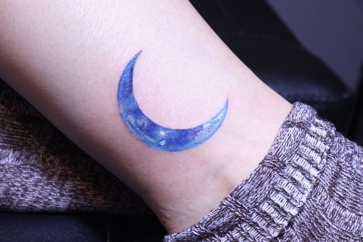 a woman's arm with a blue crescent tattoo on the left side of her arm