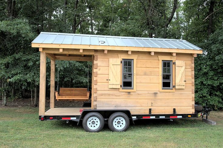 a tiny house on wheels in the grass with a porch and swing set attached to it