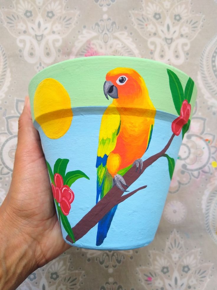 a hand holding a painted pot with a bird on it