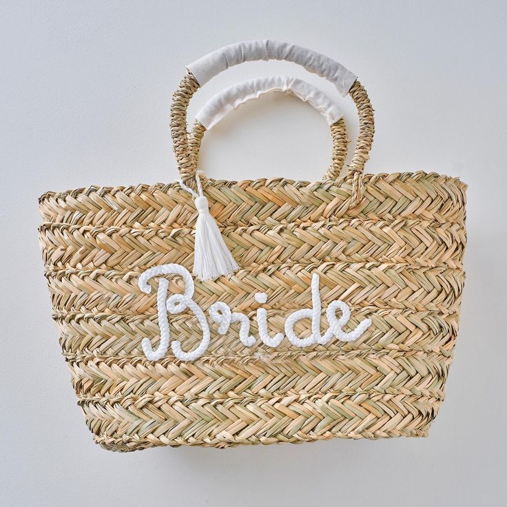 a straw bag with the word bride written on it and a tasseled handle