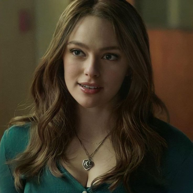 a woman with long brown hair wearing a green sweater and necklace in front of a mirror