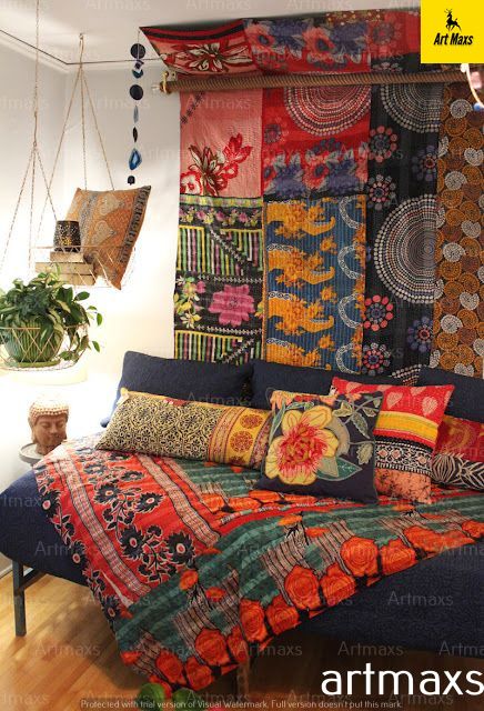 a bed covered in lots of colorful pillows and blankets next to a potted plant