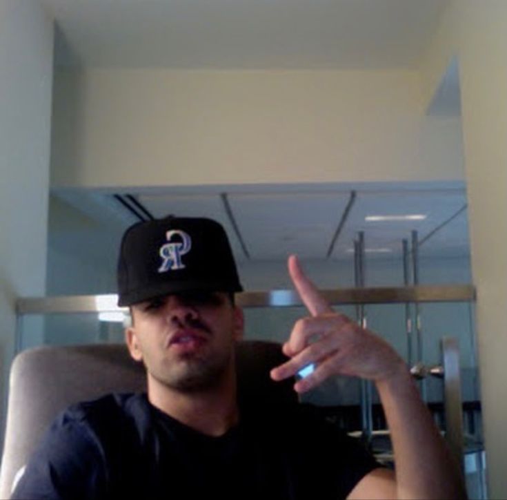 a man sitting in a chair wearing a baseball cap and pointing to the side with his finger