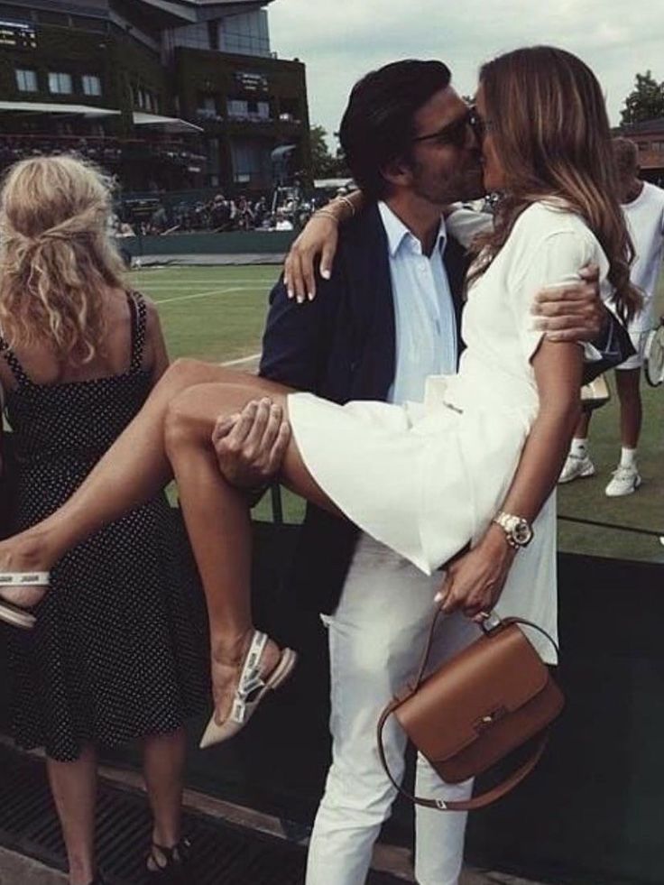 a man and woman kissing while standing on a tennis court with other people in the background