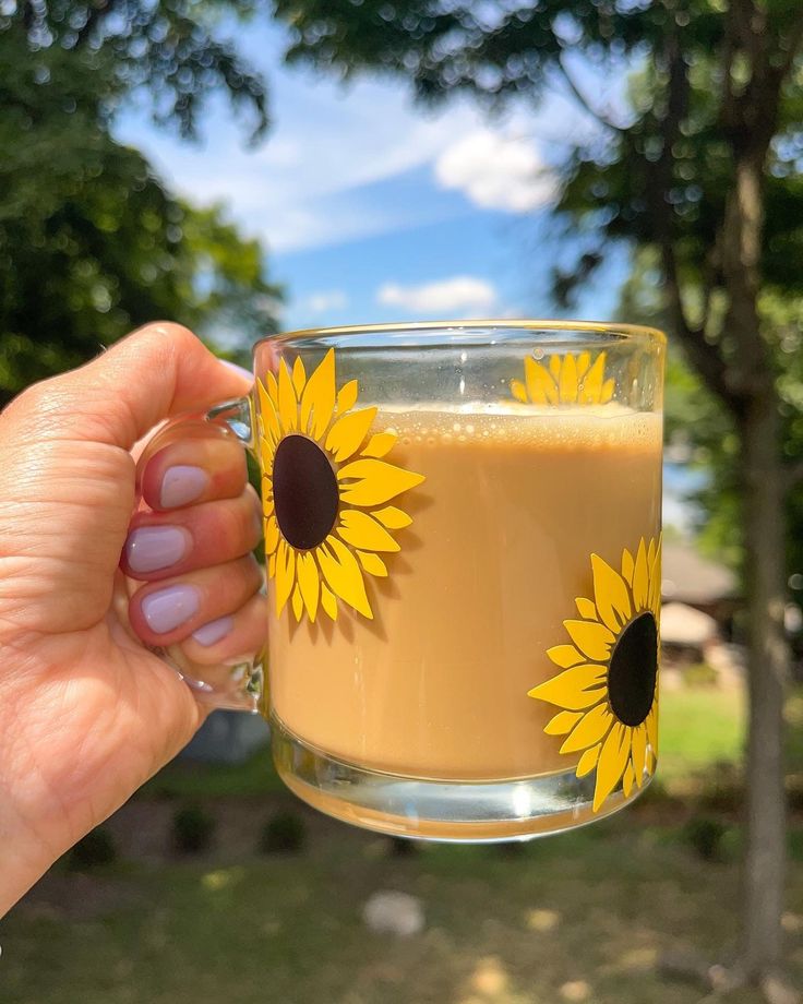 a hand holding a glass with a drink in it and two sunflowers on the side