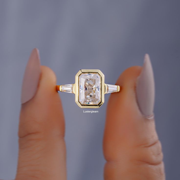 a woman's hand holding an engagement ring with a diamond in the center and two baguettes on each side