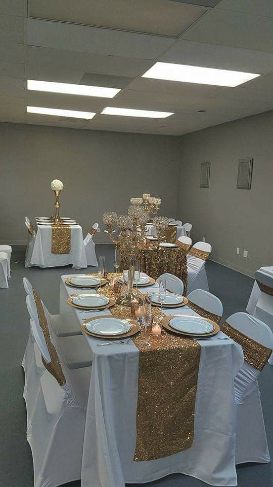 a banquet room set up with white and gold table cloths, silver chairs, and centerpieces