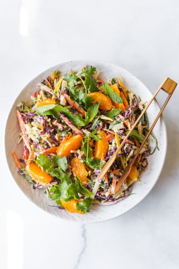 a salad with oranges, carrots and cilantro in a white bowl