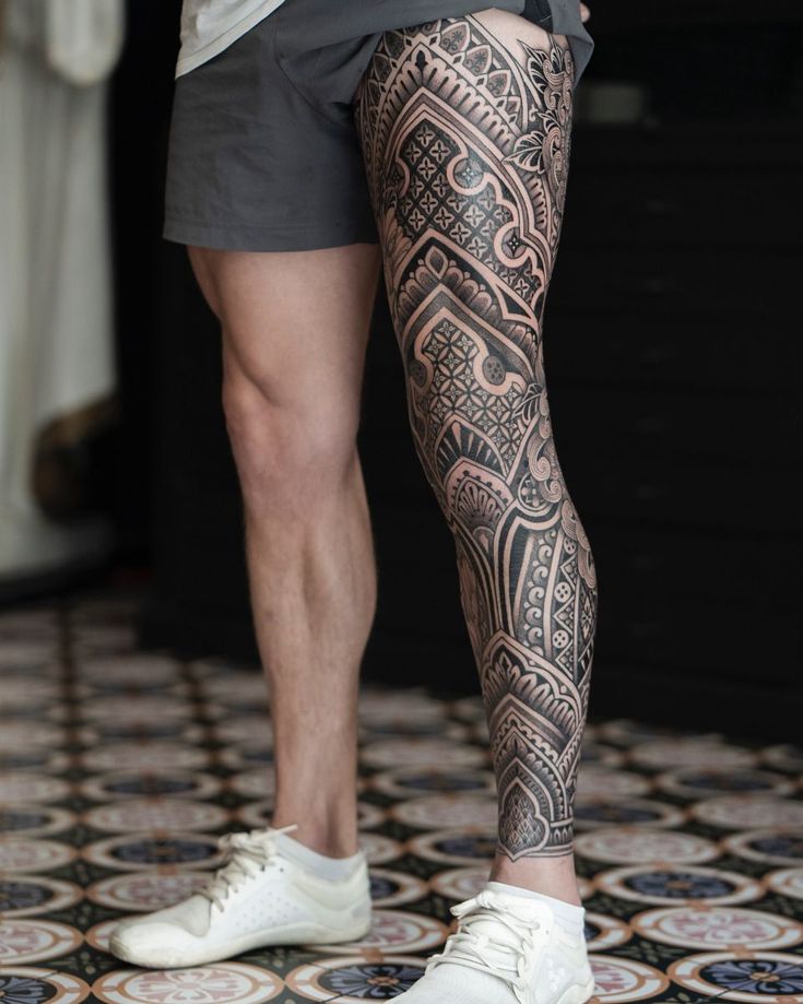 a man with tattoos on his legs and leggings is standing in front of a tiled floor