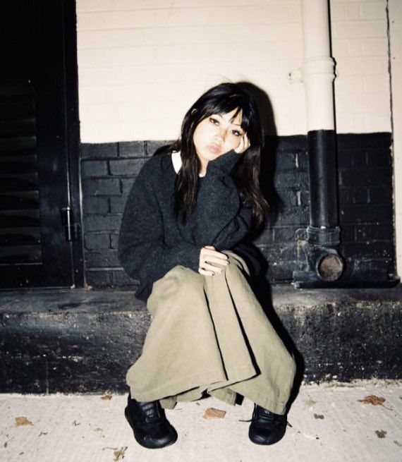 a woman sitting on the ground with her hand under her face and holding a bag