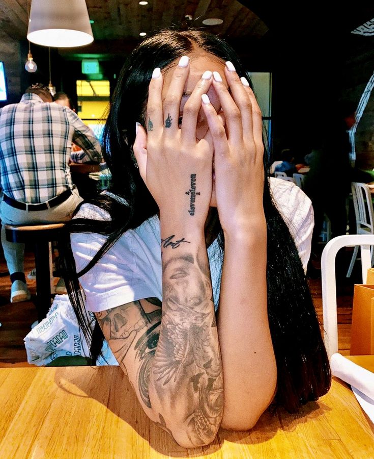 a woman sitting at a table covering her face with both hands