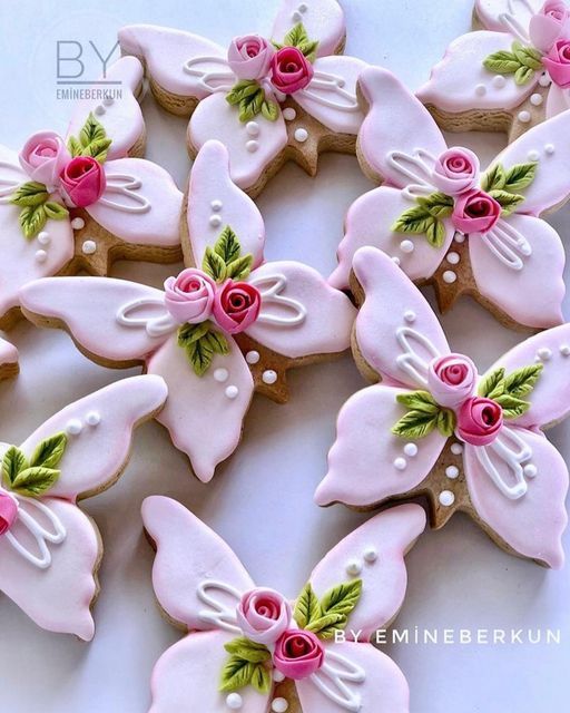 decorated cookies are arranged in the shape of butterfly's wings and pink flowers with green leaves