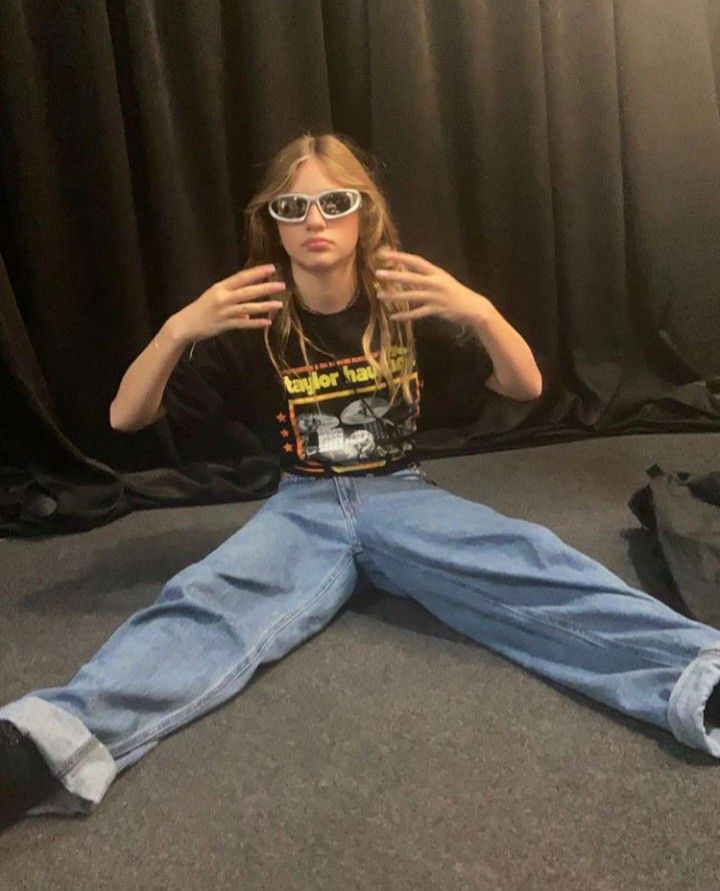 a woman sitting on the floor with her hands behind her head and wearing sunglasses over her eyes