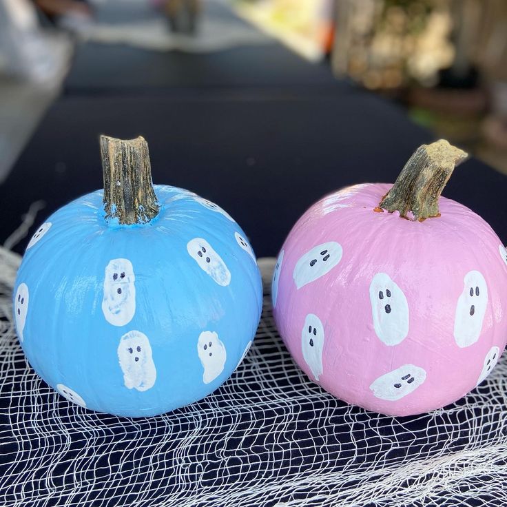 two painted pumpkins sitting on top of a blue cloth covered table next to each other