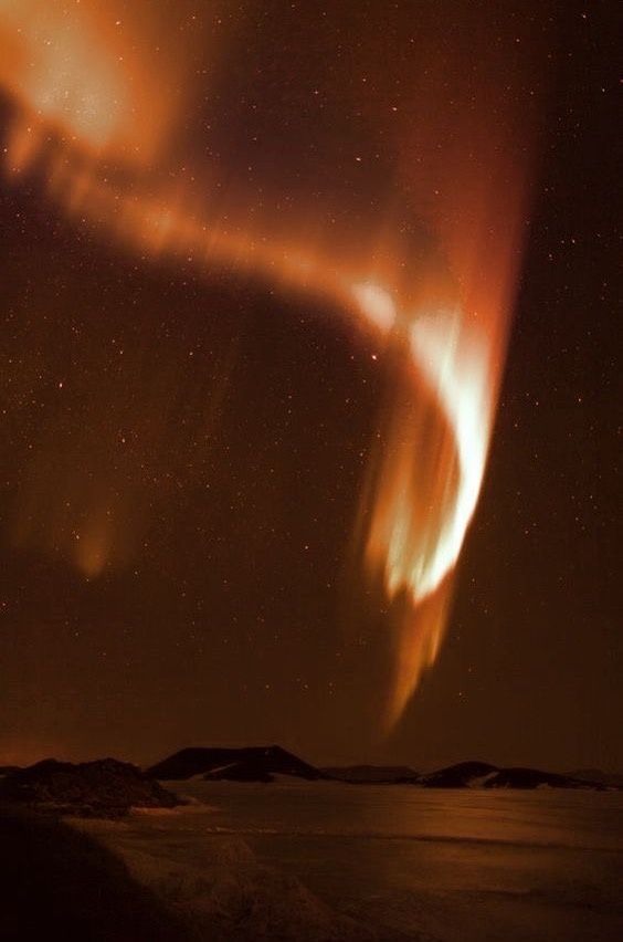 an aurora bore is seen in the night sky over water and snow covered mountains with bright orange lights