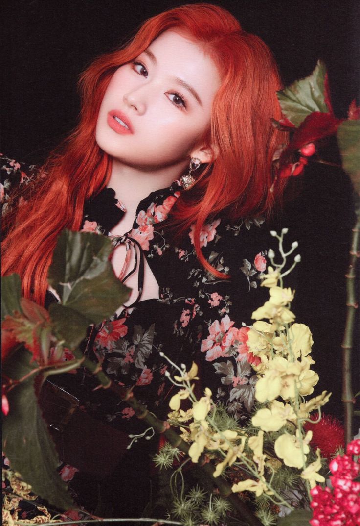 a woman with red hair and flowers in front of a black background is looking at the camera