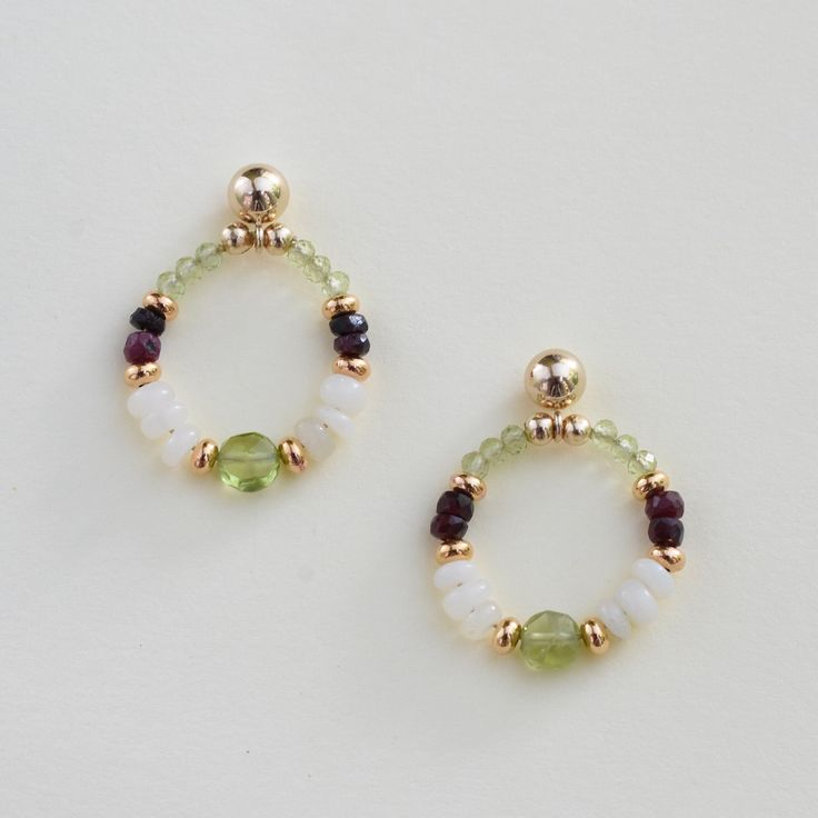 Our white opal, ruby, and peridot earrings are packed with gemstones.  A unique July, August or October birthstone gift OR 14th, 15th, 16th or 40th-anniversary gift.  The 14k gold-filled post earrings feature a peridot bead at the base and top of the hoop, complemented by white opals, gold-plated brass, and contrasting red rubies.  The pair is lightweight and long-lasting.  A lovely personal treat or gift for your wife, mom, or friend.   The jewelry arrives wrapped for easy gifting and includes Gemstone Accented Earrings For May Birthstone, May Birthstone Earrings With Natural Stones For Gift, Small Hoop Birthstone Earrings For Anniversary, Dainty Hoop Earrings With May Birthstone, Natural Stone Earrings For May Birthstone Gift, Dainty May Birthstone Hoop Jewelry, May Birthstone Hoop Gemstone Jewelry, May Birthstone Earrings With Gemstone Accents, May Birthstone Earrings With Natural Stones