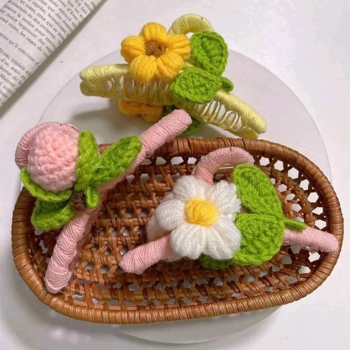 two crocheted flowers sitting on top of a wicker basket next to a book