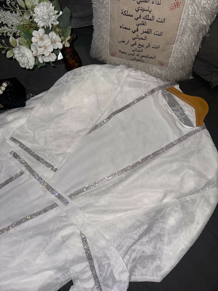 Elevate your style for special occasions with the Noor White Abaya, perfect for nikah ceremonies or parties. Its intricate diamond detailing and elegant design exude sophistication, making it the ideal choice for memorable moments. With a slip dress inner layer, matching hijab, and a dazzling diamond-detailed belt, this abaya ensures you stand out with timeless grace and beauty. Luxury White Dress For Wedding Night, Elegant Dabka Thobe For Eid, Elegant Long Sleeve Thobe With Dabka Embroidery, Elegant Long Sleeve Thobe With Dabka, Elegant Floor-length Abaya With Dabka, Elegant Dabka Embroidered Thobe For Festive Season, Wedding Abaya For Eid In Maxi Length, Elegant Dabka Thobe For Festive Season, Elegant Floor-length Dabka Abaya