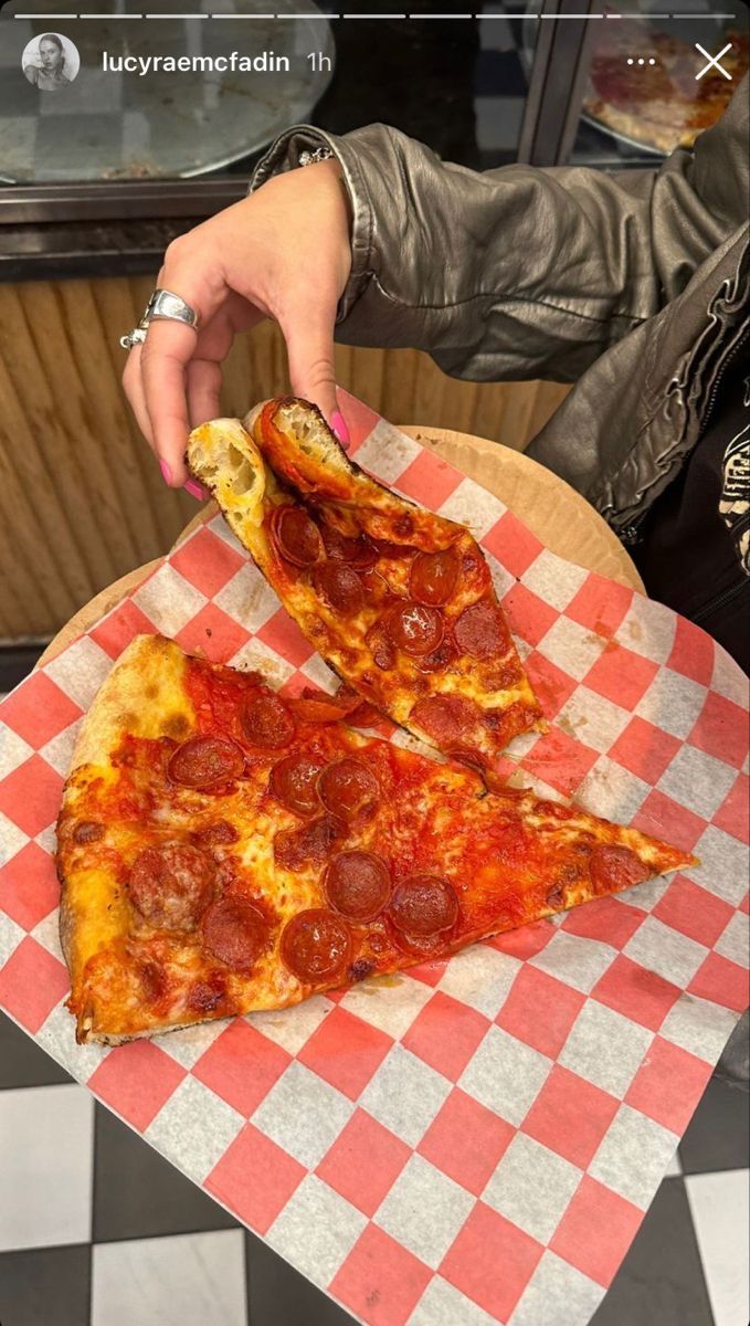 two slices of pepperoni pizza sitting on top of a checkered paper plate in front of a woman's hand